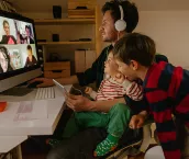 Photo of a man working from home, with his sons keeping him company, having a video conference call