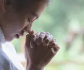 A woman with clasped hands praying.