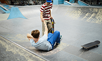One of guys helping his fallen friend to stand up during incident at parkour area or lesure center