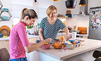 A young woman with hearing aids talking to her mother in the kitchen. They have a breakfast and enjoying the time they spending together.
