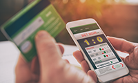 Man betting on sports with credit card, over shoulder view on hand with smartphone