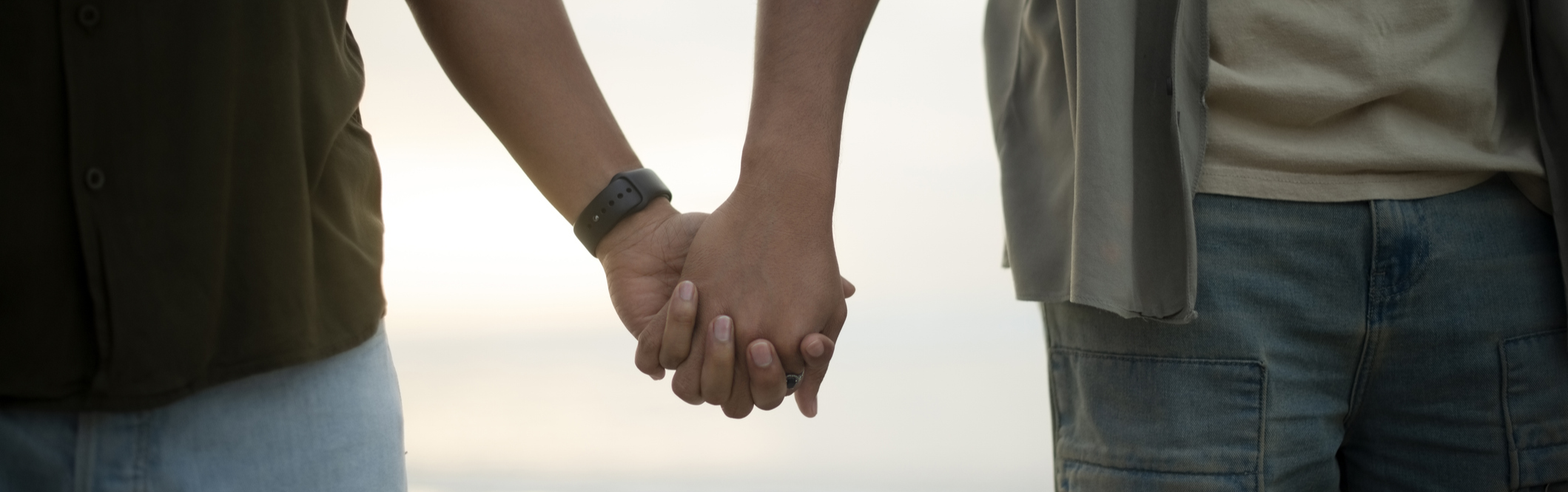 Close up shot of 2 men holding hands on the beach