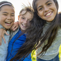 A small group of Elementary children huddle in closely to one another as they pose for a portrait. They are each dressed casually and are smiling as they spend the time together.