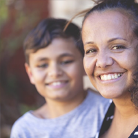 Aboriginal Family portrait with 1 parent and 2 children. They are sitting on the front porch. Everyone is happy and smiling.