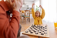 A delighted granddaughter raises her arms in celebration after winning a game of chess at home.