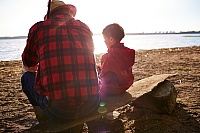 Fisherman and his grandson sitting on riverbank at sunset