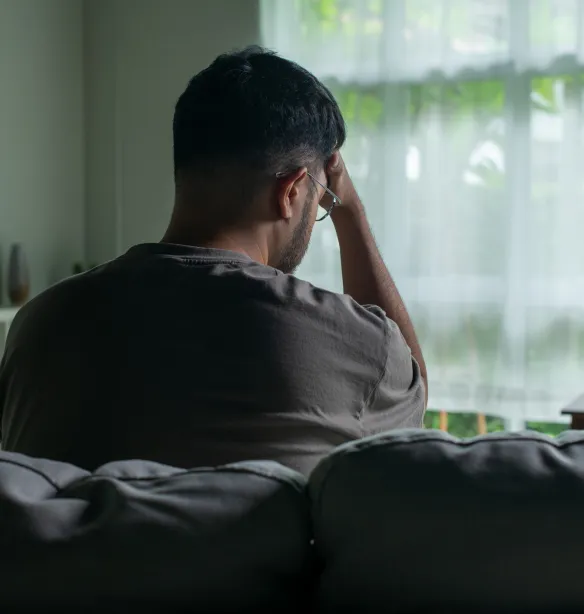 Young Asian man sitting on a sofa at home, looking sad and exhausted, struggling with depression and mental health issues.