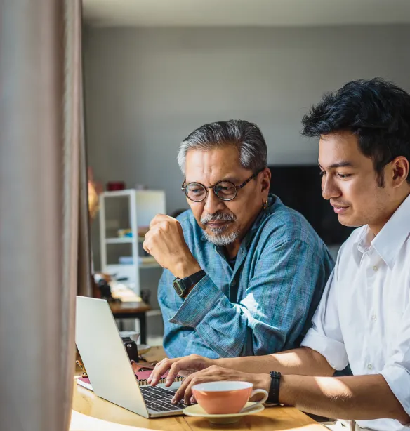 Asian senior father and his adult son using laptop computer while sitting at home