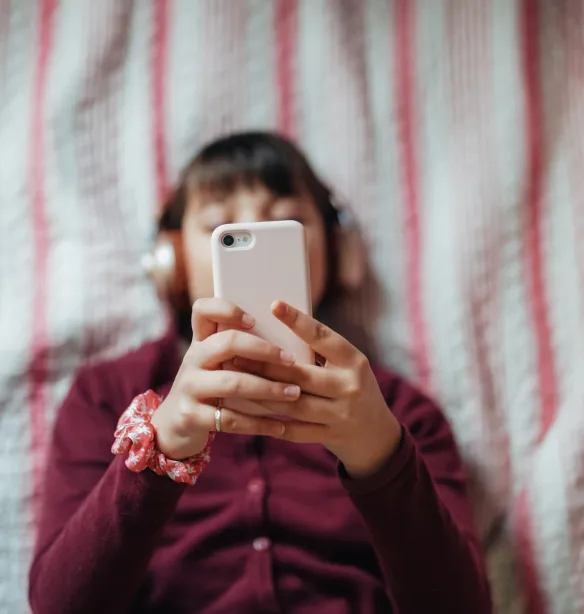 A teenager lying in bed looking at her phone.
