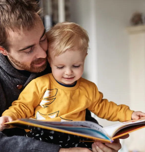Cropped shot of an adorable little boy reading a book while sitting with his father at home