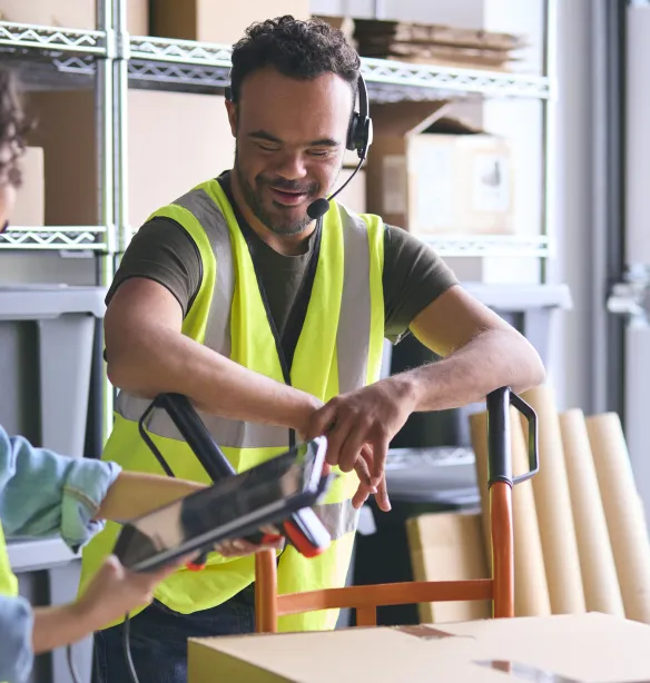 2 workers in a distribution warehouse wearing high vis clothing using a digital tablet.