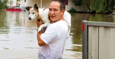 Man holding a dog on his shoulders as he stands in waist deep flood waters. 