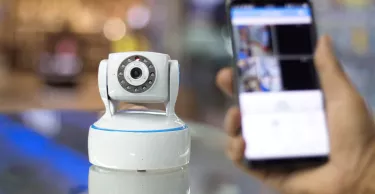 CCTV camera in the foreground and a hand holding a mobile phone in the background