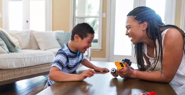 The young boy with Down Syndrome enjoys play therapy with his therapist at home.