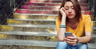 Teen girl dressed in yellow t-shirt sitting on stairs and is breaking up with her boyfriend through text messages.