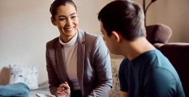Happy psychologist talking to man with down syndrome while visiting him at home.