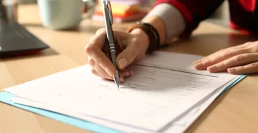 Close up of student girl hand filling out form on a desk at home at night