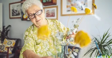 Senior woman arranging flowers in a vase at home.