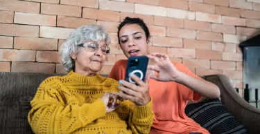 Granddaughter helping grandmother to use the mobile phone at home.