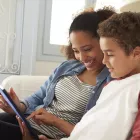 Mother and son sitting on sofa using digital tablet