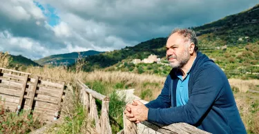Side view of a happy thoughtful bearded mature man contemplating mountain nature with cloudy sky near wooden footbridge. Concept of leisure activities,tourism, lifestyle e nature