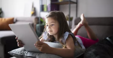 little girl laying on sofa at home and using digital tablet.
