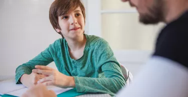 Elementary aged boy doing homework at the dining table and looking at his father