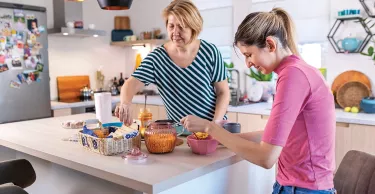 A young woman with hearing aids talking to her mother in the kitchen. They have a breakfast and enjoying the time they spending together.