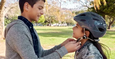 Shot of a young boy helping to secure his sister’s helmet before she rides her bicycle in the park