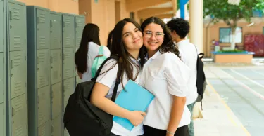 Portrait of two cheerful teenage girls wearing school uniform and embracing each other in a school hallway.
