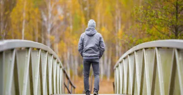 One young man in gray clothes slowly walking on bridge at natural park in colorful autumn day.