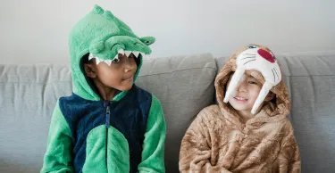 Two boys in animal costumes sitting together on a sofa indoors.