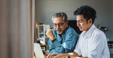 Asian senior father and his adult son using laptop computer while sitting at home