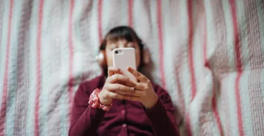 A teenager lying in bed looking at her phone.