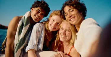 Young man holding phone and taking photo of himself with three friends