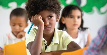 A photo of a young boy in a classroom and behind him are two young children blurred out in the background
