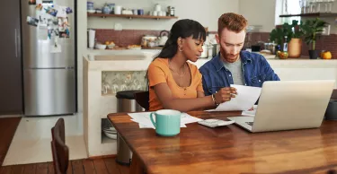 A couple reviewing paperwork and looking through the laptop on the kitchen table