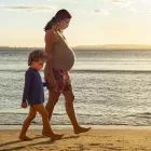 Pregnant mother exercising at the beach, holding her toddler's son hand by the sea, during sunset.