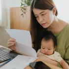 Mother sitting with baby in her lap, using laptop to check finances at home.