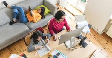 Young mother working on her computer with her daughters playing on their mobile devices