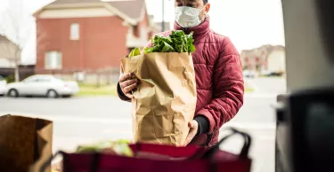 Mature man wearing protection mask, unloading grocery from car trunk