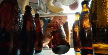 Young woman takes cold refreshing beer from out the fridge, inside view from fridge of hand holding the bottle.