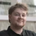 A man with light hair and a beard looks at the camera smiling.