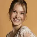 A girl with blonde hair smiles wearing a floral top