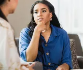An empathetic mid adult female counselor sits with her hand on her chin as she listens to the unrecognizable mid adult female client. An empathetic mid adult female counselor sits with her hand on her chin as she listens to the unrecognizable mid adult female client.