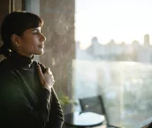 Young woman standing at a window at sunset contemplating at home