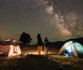 Mother and son tourists resting at camping in mountains at night sky full of stars and Milky way.