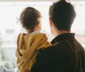 Rear view of dad holding his baby boy looking out of the window at home.