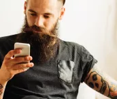 Young bearded tattooed man using mobile phone.