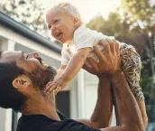 Shot of a father playing with his baby boy while standing outside his house